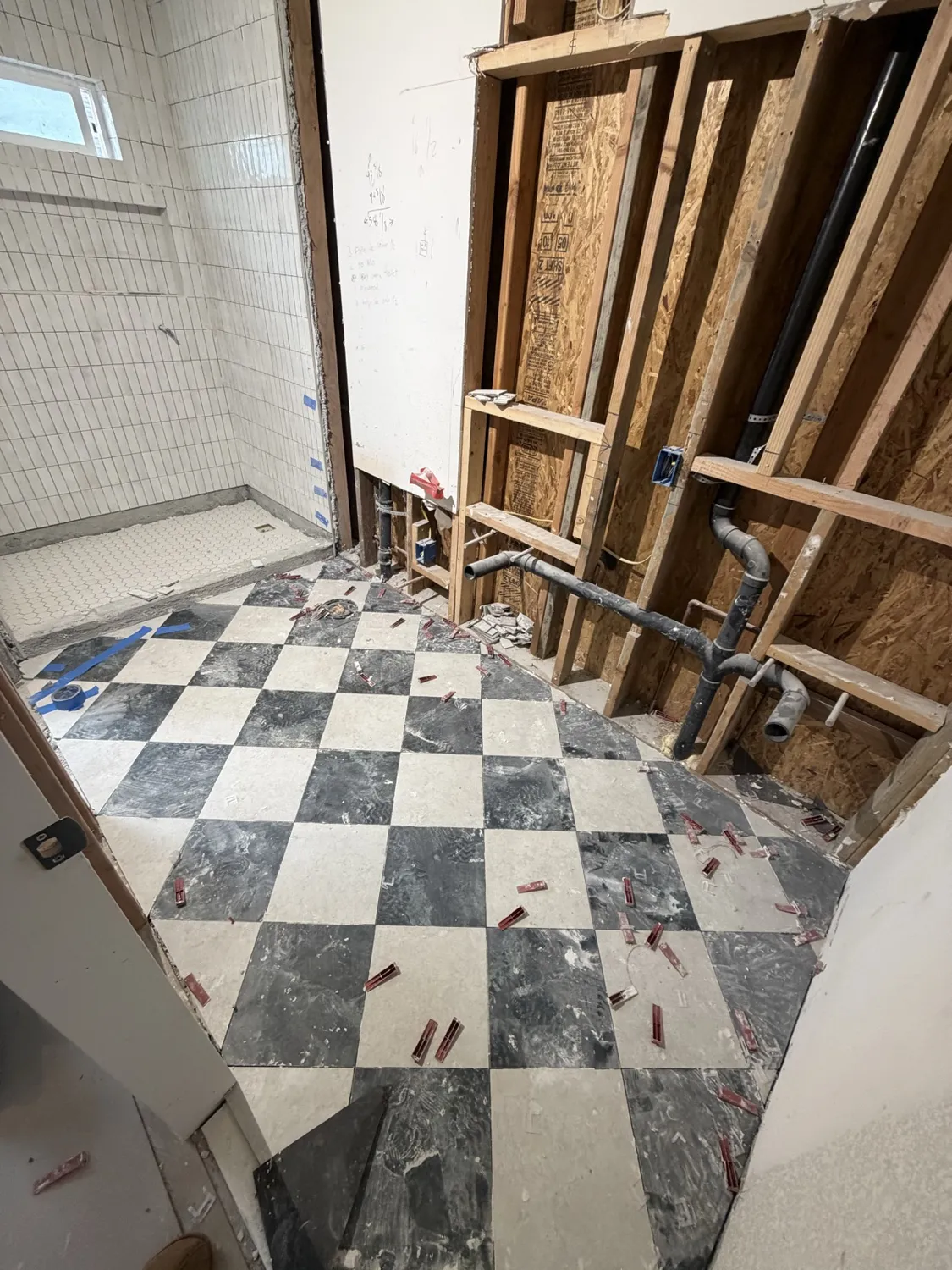 Bathroom remodel in progress with new checkerboard tile, open framing and plumbing